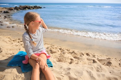 Photo of Little girl in sunglasses on sandy beach near sea. Space for text