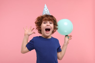 Photo of Emotional little boy in party hat with balloon on pink background
