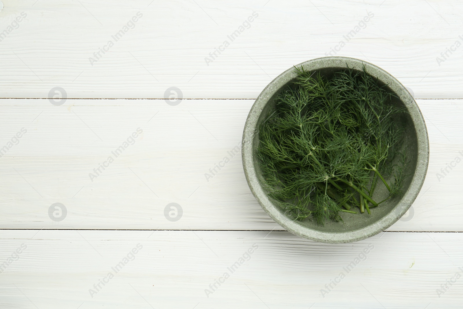 Photo of Bowl of fresh green dill on white wooden table, top view. Space for text