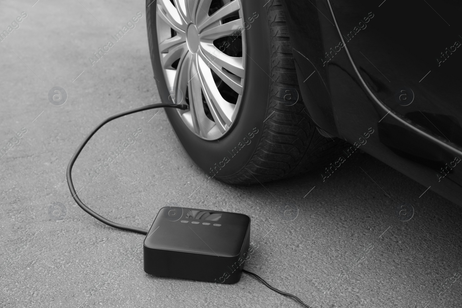 Photo of Inflating car tire with portable air pump outdoors