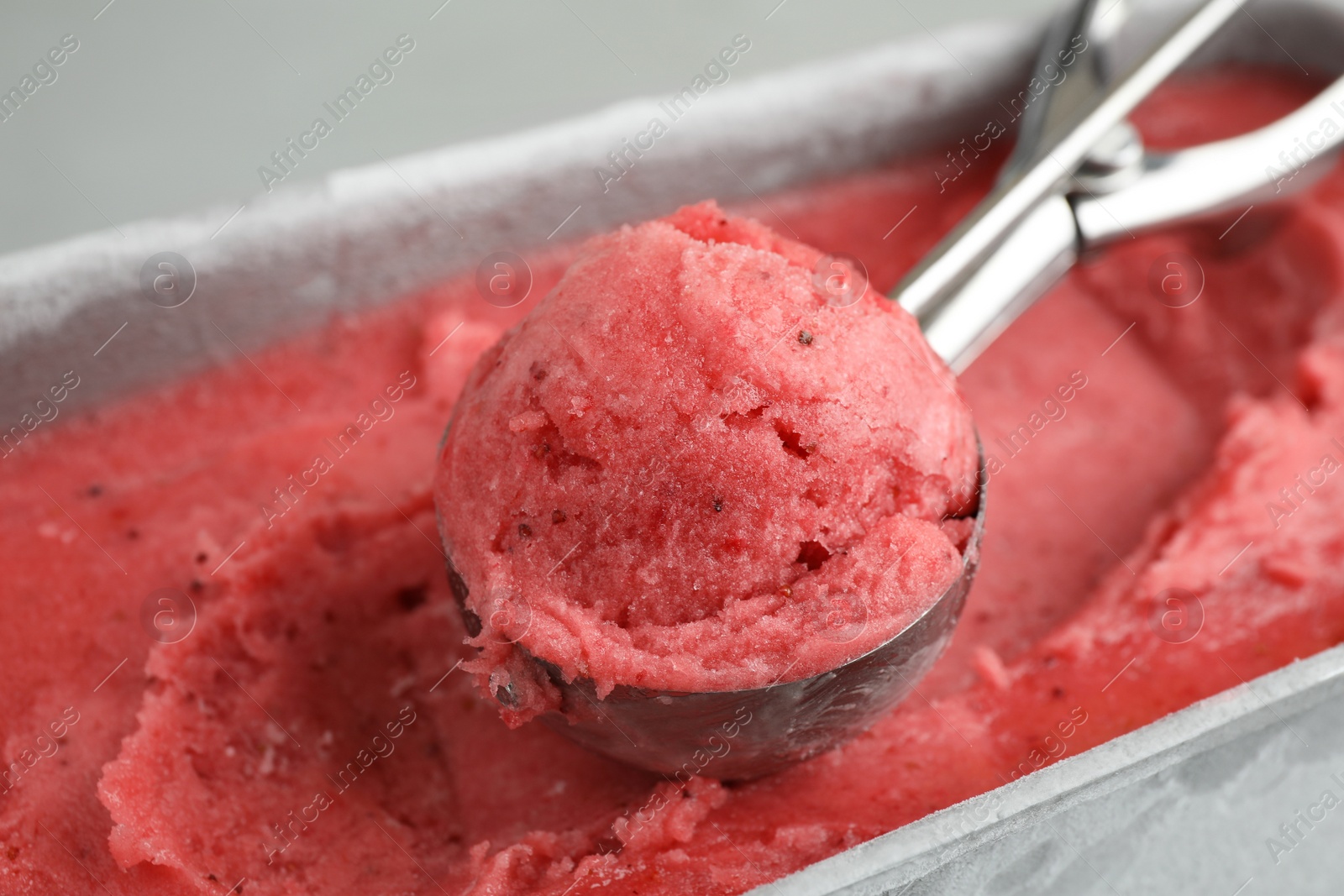 Photo of Container with delicious pink ice cream and scoop, closeup