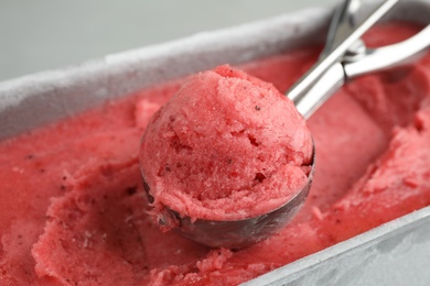 Photo of Container with delicious pink ice cream and scoop, closeup