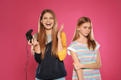 Young woman and teenage girl playing video games with controllers on color background