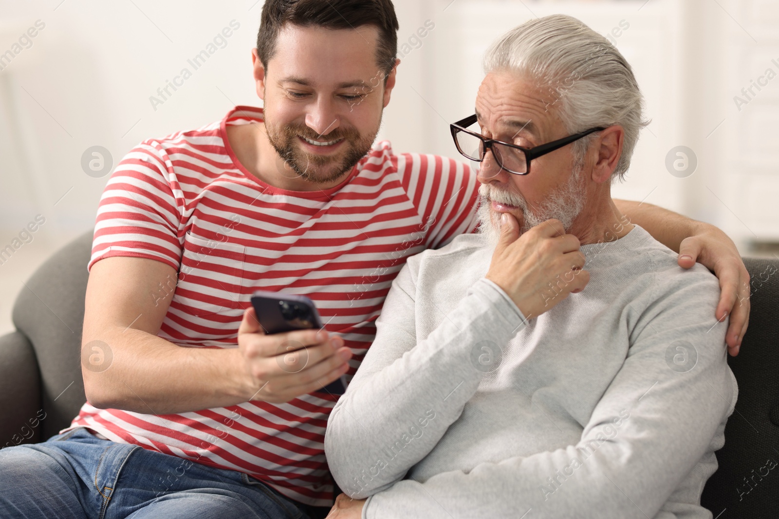 Photo of Happy son and his dad watching something on smartphone at home
