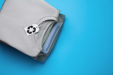 Photo of Stack of clothes with recycling label on light blue background, top view. Space for text
