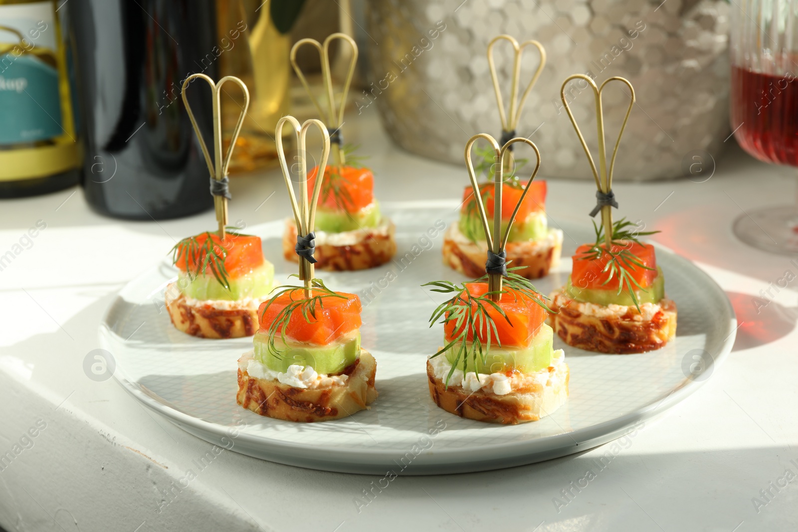 Photo of Tasty canapes with salmon, cucumber, bread and cream cheese on white table