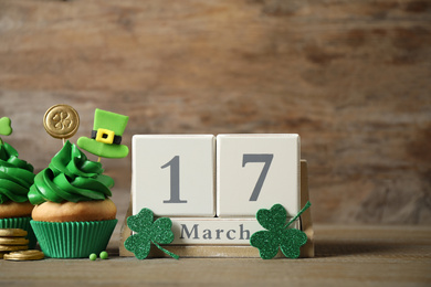 Photo of Decorated cupcakes, wooden block calendar and coins on table. St. Patrick's day celebration