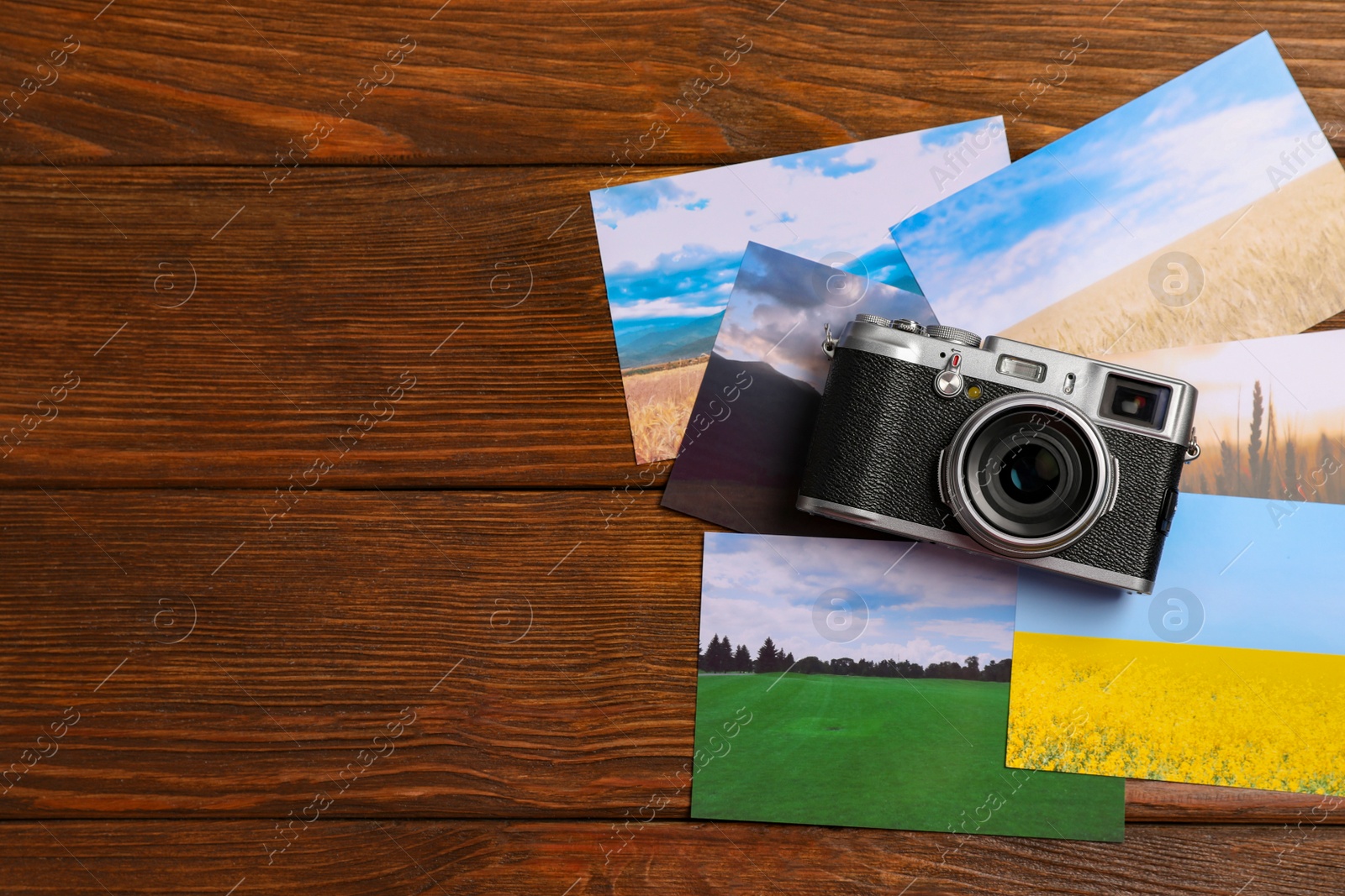 Photo of Vintage photo camera and beautiful printed pictures on wooden table, flat lay with space for text. Creative hobby