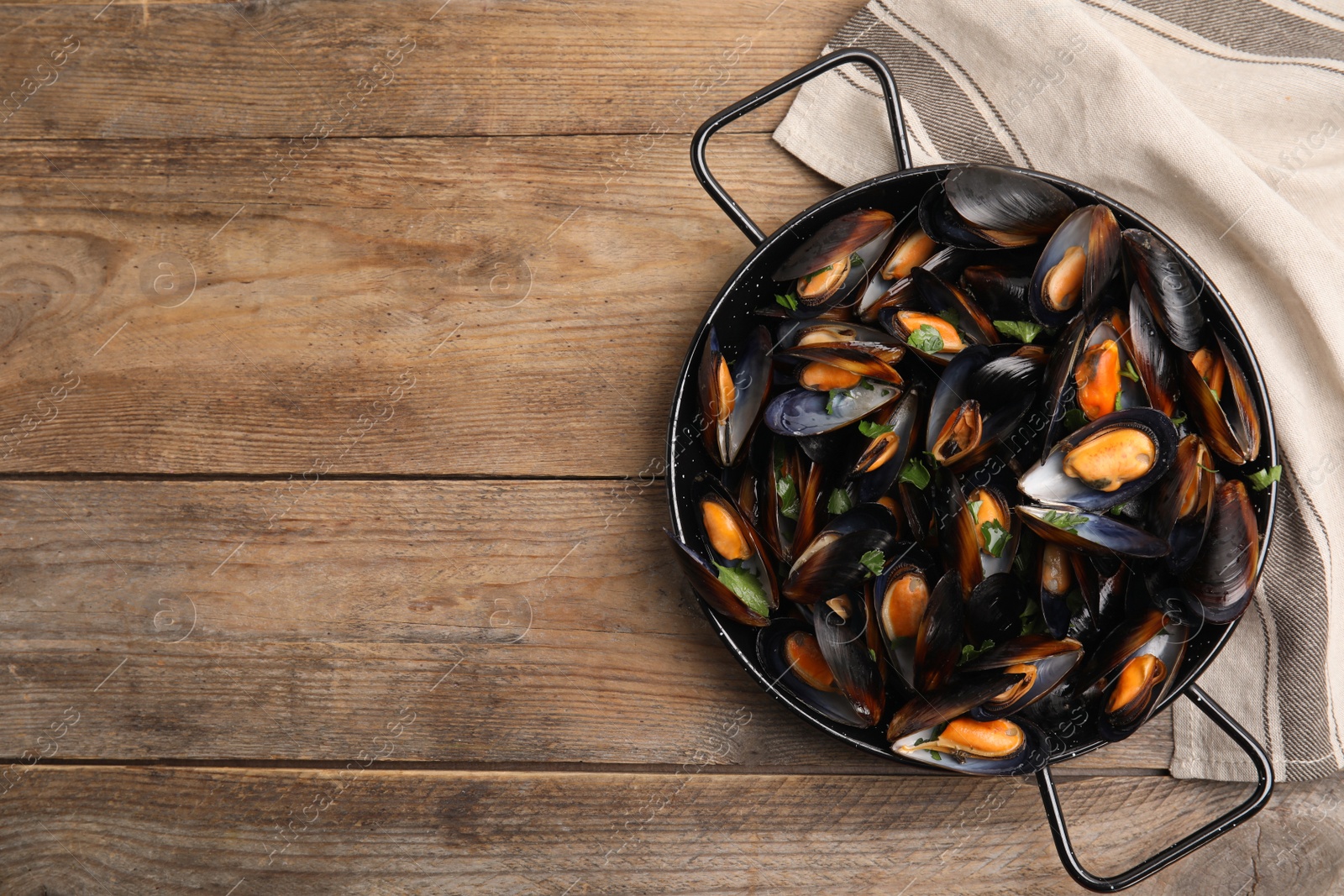 Photo of Pan of cooked mussels with parsley on wooden table, top view. Space for text