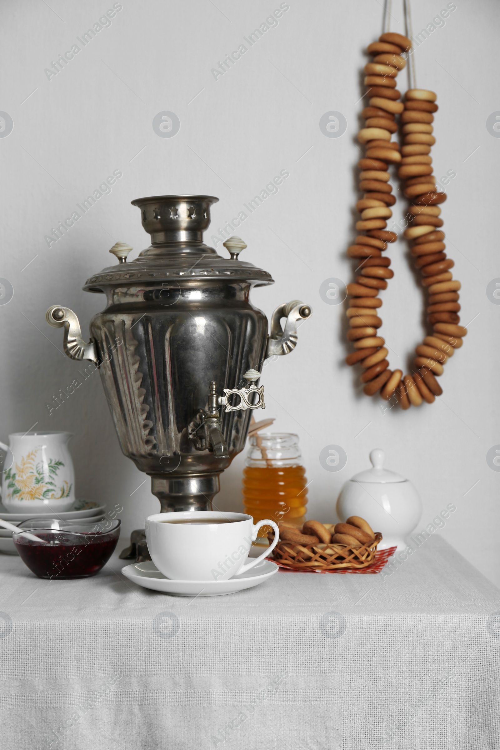 Photo of Composition with delicious ring shaped Sushki (dry bagels) and tea on white tablecloth near wall