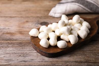 Board with delicious mozzarella cheese balls on wooden table. Space for text