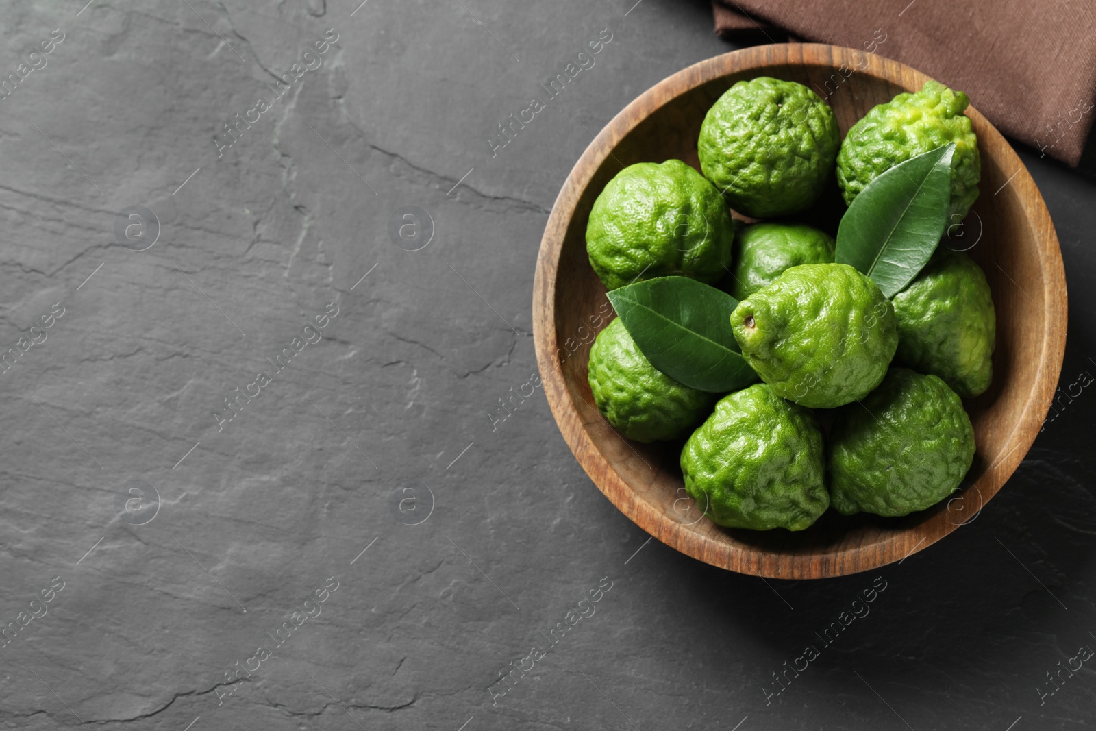 Photo of Fresh ripe bergamot fruits with leaves in bowl on black table, top view. Space for text