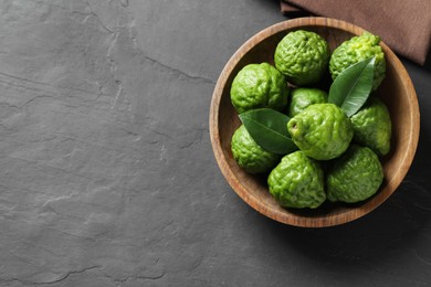 Fresh ripe bergamot fruits with leaves in bowl on black table, top view. Space for text