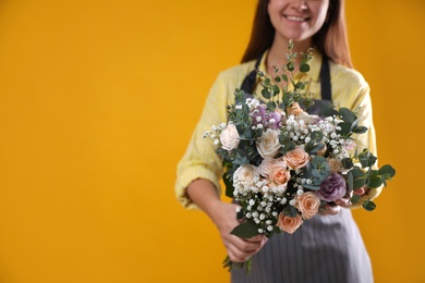 Photo of Florist holding beautiful wedding bouquet on yellow background, closeup. Space for text