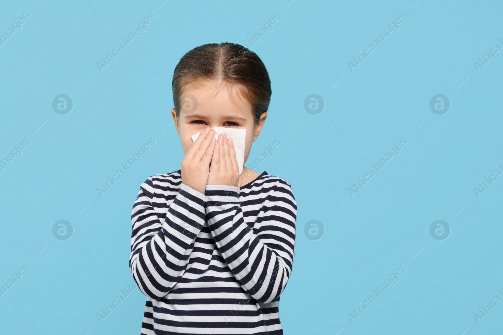 Photo of Girl blowing nose in tissue on light blue background, space for text. Cold symptoms