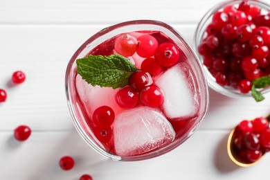 Photo of Tasty cranberry juice with ice cubes in glass and fresh berries on white wooden table, flat lay