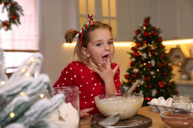 Photo of Cute little girl having fun while making dough for Christmas cookies in kitchen