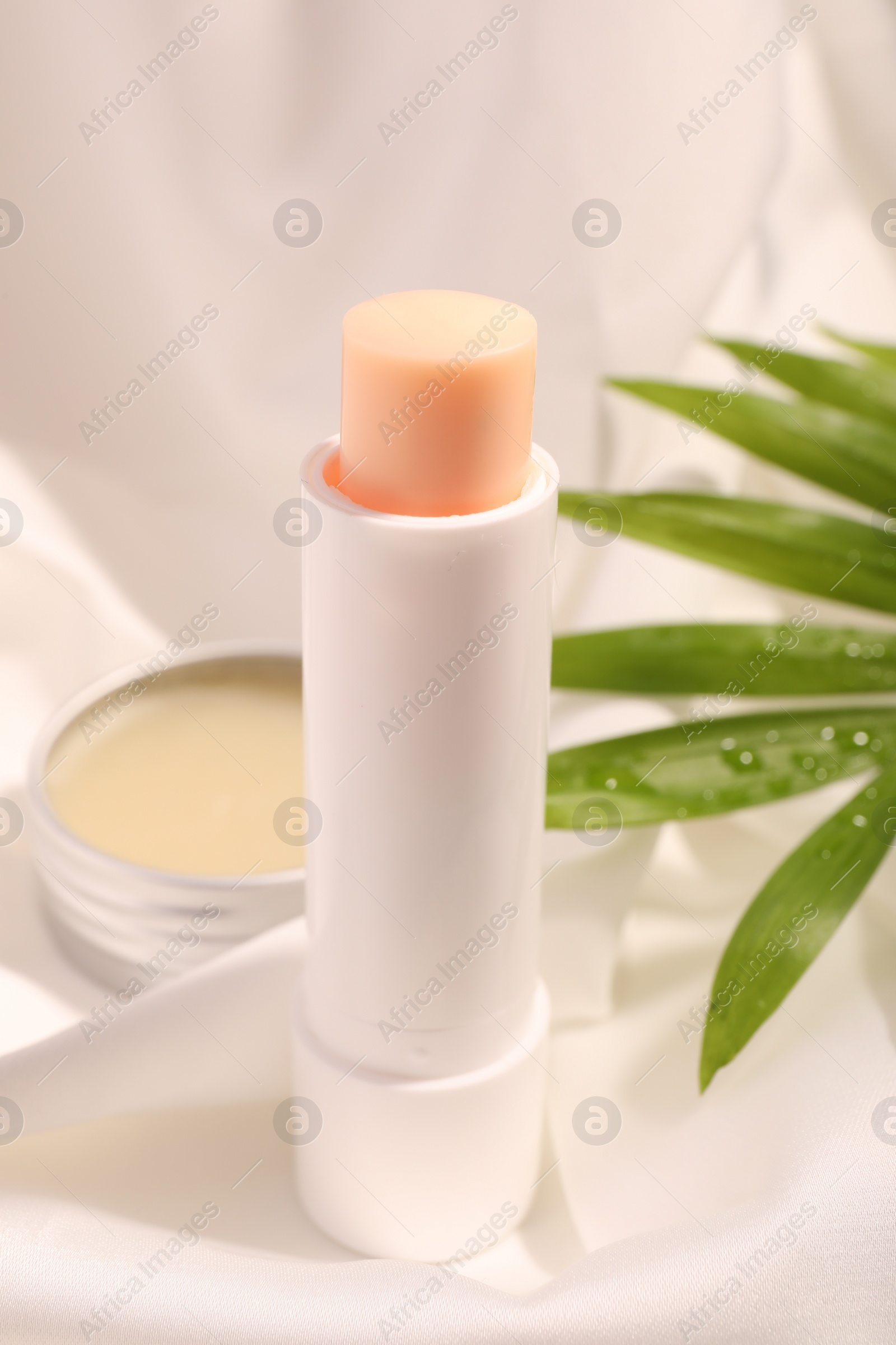 Photo of Lip balms and palm leaf on white fabric, closeup