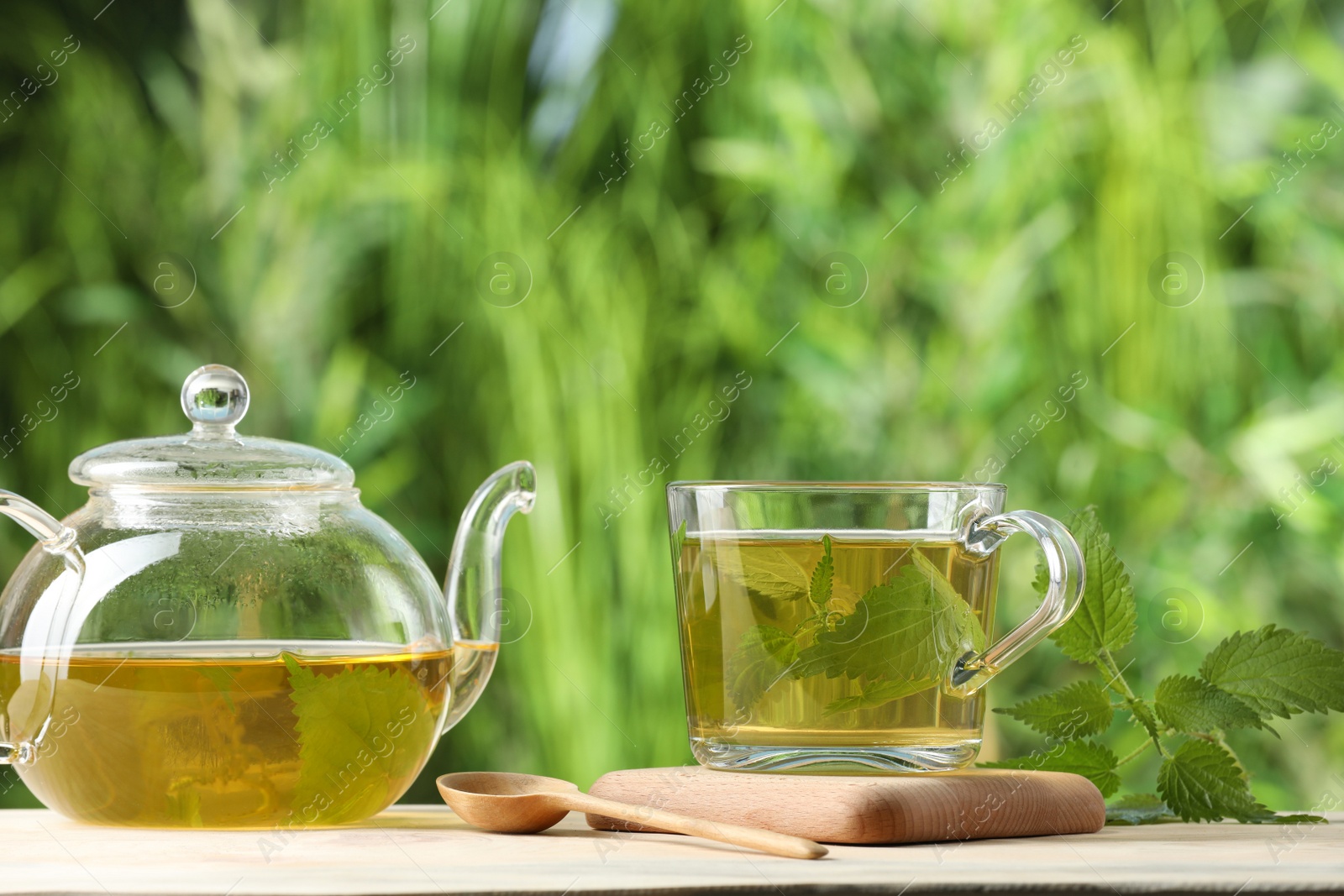 Photo of Aromatic nettle tea and green leaves on table outdoors