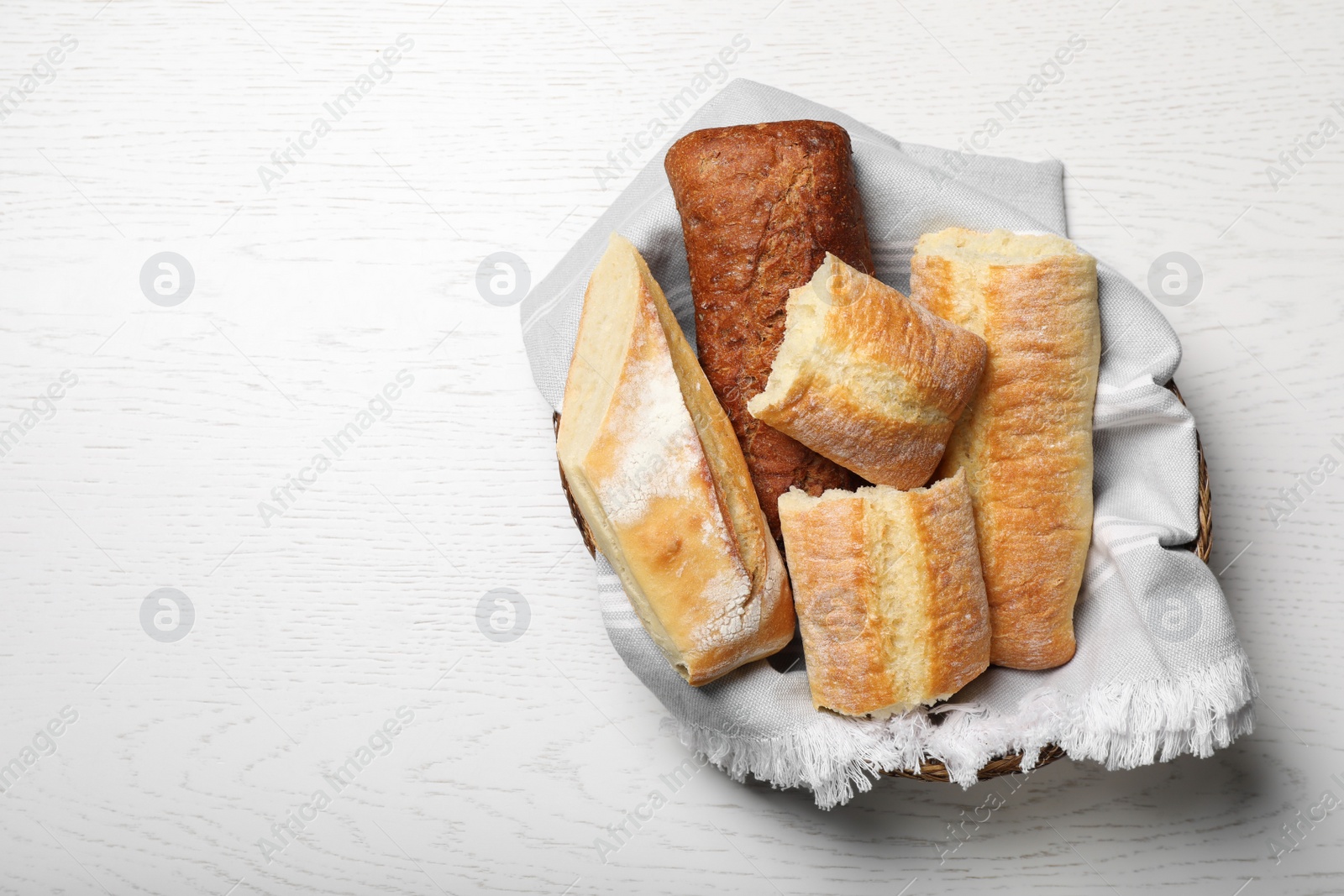 Photo of Different tasty baguettes in basket on white wooden table, top view. Space for text