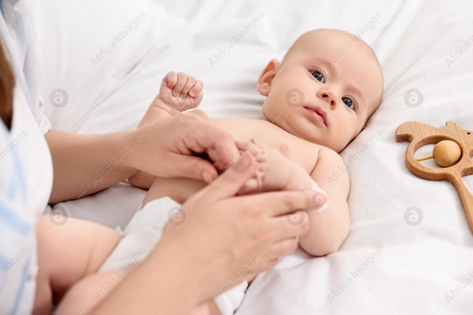 Photo of Woman applying body cream onto baby`s skin on bed, closeup