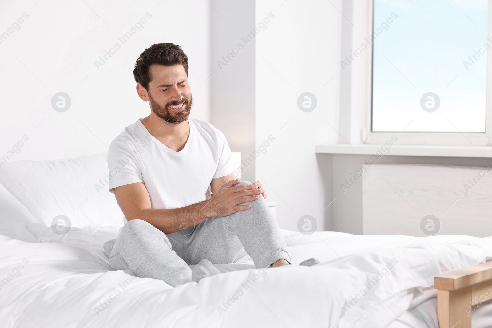 Photo of Man suffering from leg pain on bed at home