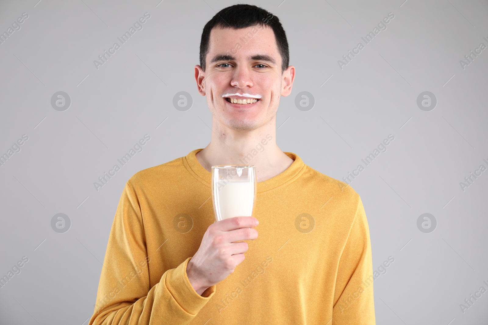 Photo of Happy man with milk mustache holding glass of tasty dairy drink on gray background