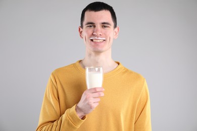 Happy man with milk mustache holding glass of tasty dairy drink on gray background