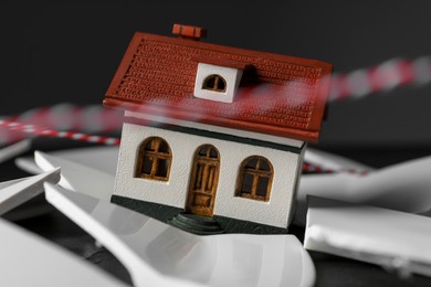 Photo of House model and broken dishes on black table depicting destruction after earthquake, closeup