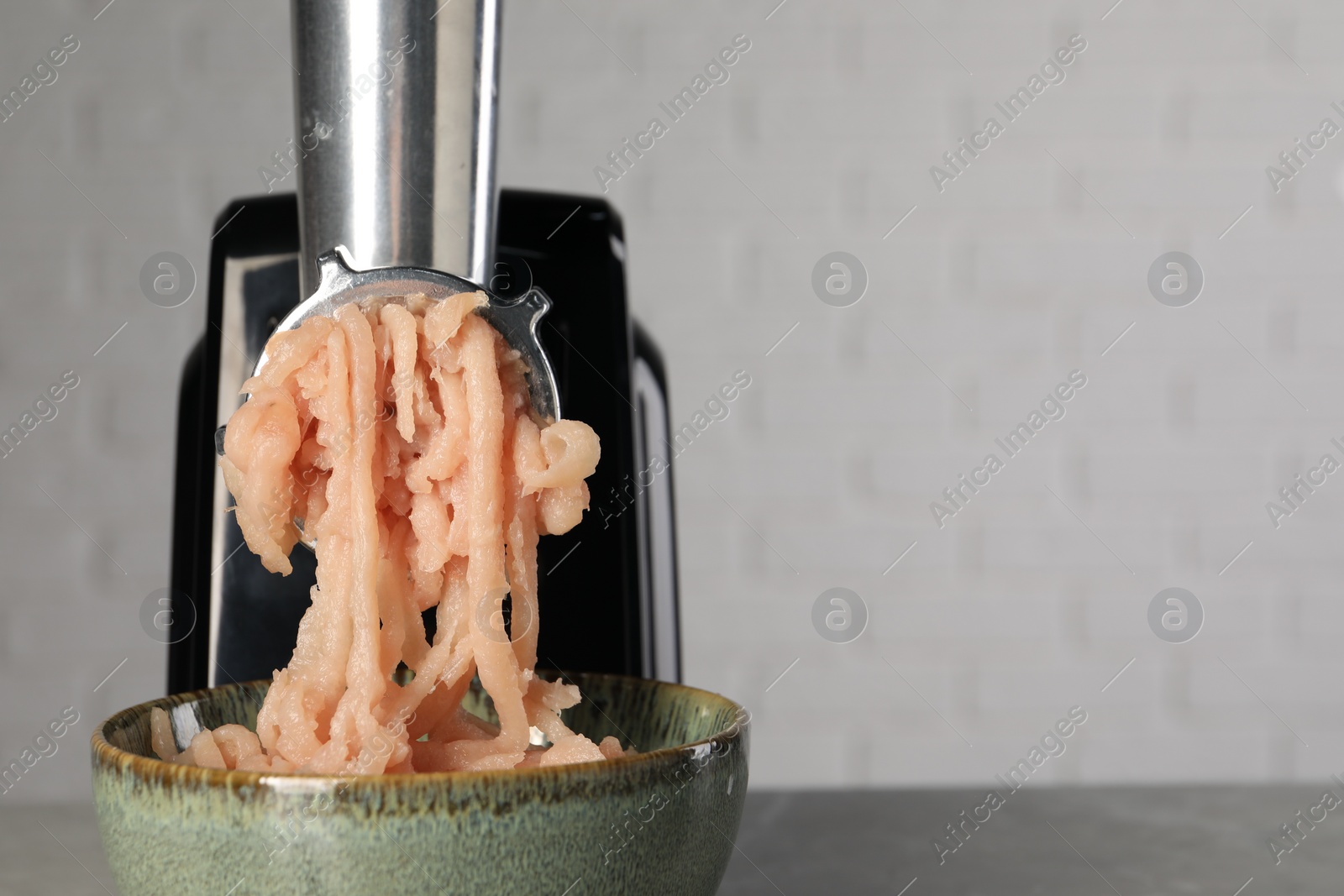 Photo of Electric meat grinder with chicken mince on table near light wall, closeup. Space for text