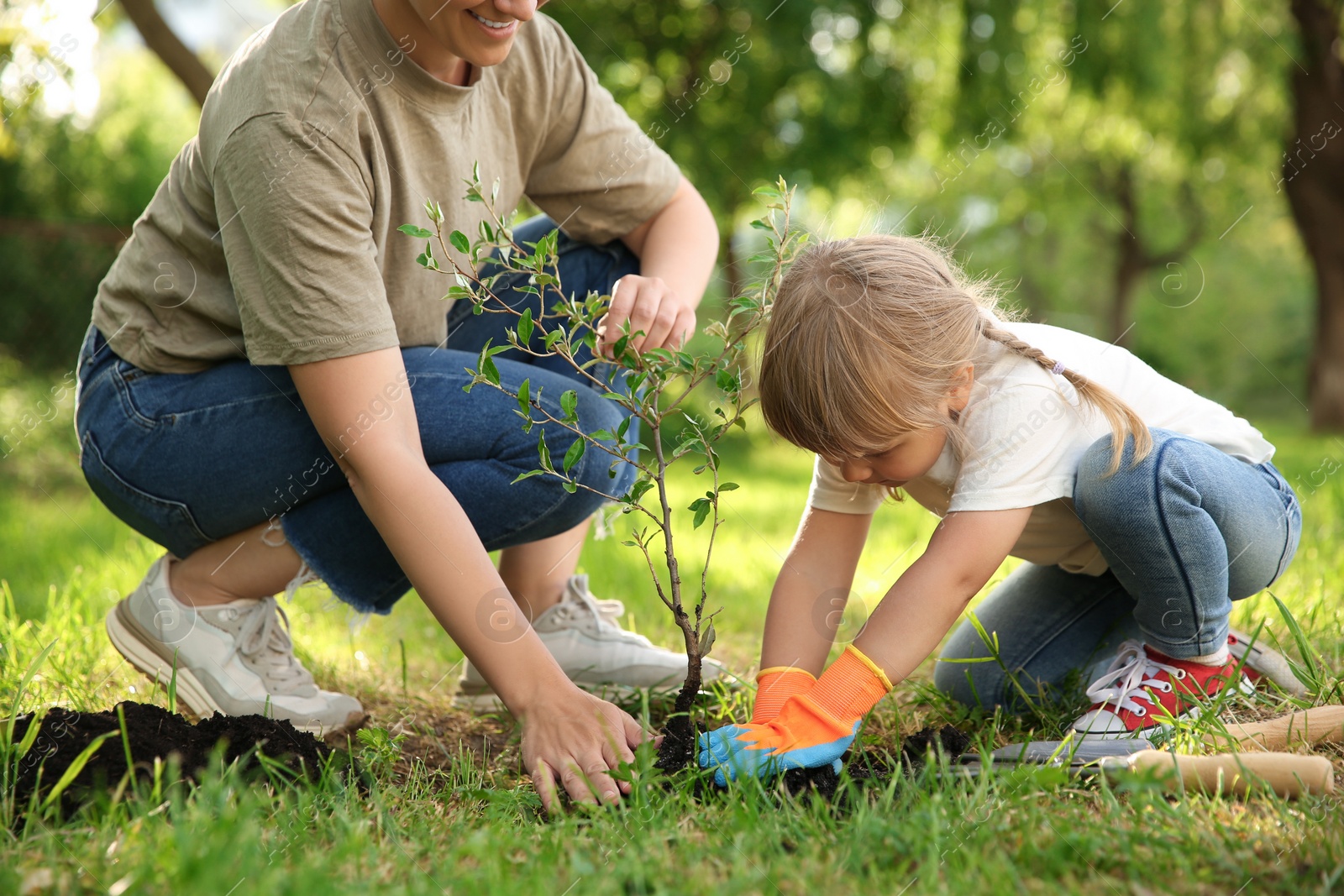 Photo of Mother and her daughter planting tree together in garden