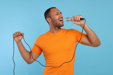 Photo of Handsome man with microphone singing on light blue background