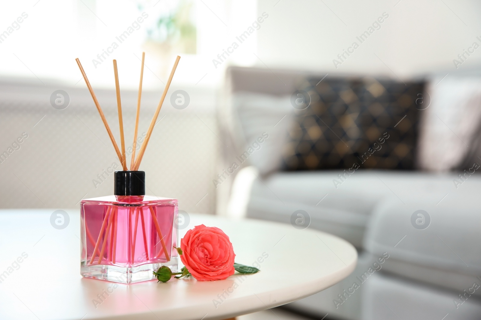 Photo of Aromatic reed air freshener and rose on table indoors