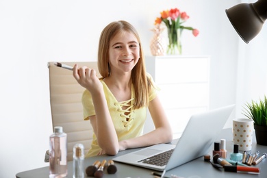 Photo of Cute teenage blogger with laptop and different cosmetics at table