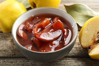 Photo of Tasty homemade quince jam in bowl and fruits on wooden table, closeup
