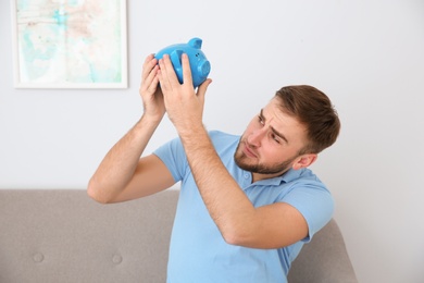 Young man with piggy bank on sofa in living room