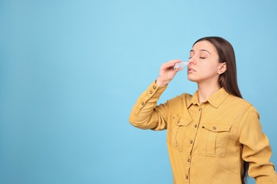 Photo of Woman using nasal spray on light blue background, space for text