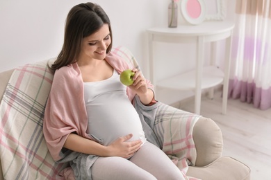 Photo of Young pregnant woman holding apple at home