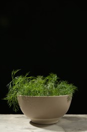 Photo of Bowl of fresh green dill with water drops on light grey table against black background. Space for text