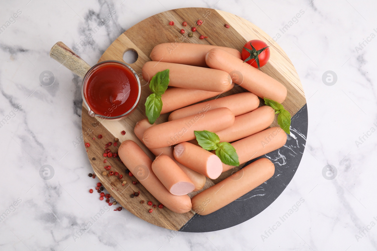 Photo of Delicious boiled sausages with spices, sauce and tomato on white marble table, top view