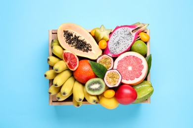 Crate with different exotic fruits on light blue background, top view