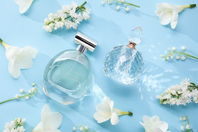 Photo of Luxury perfumes and floral decor on light blue background, flat lay