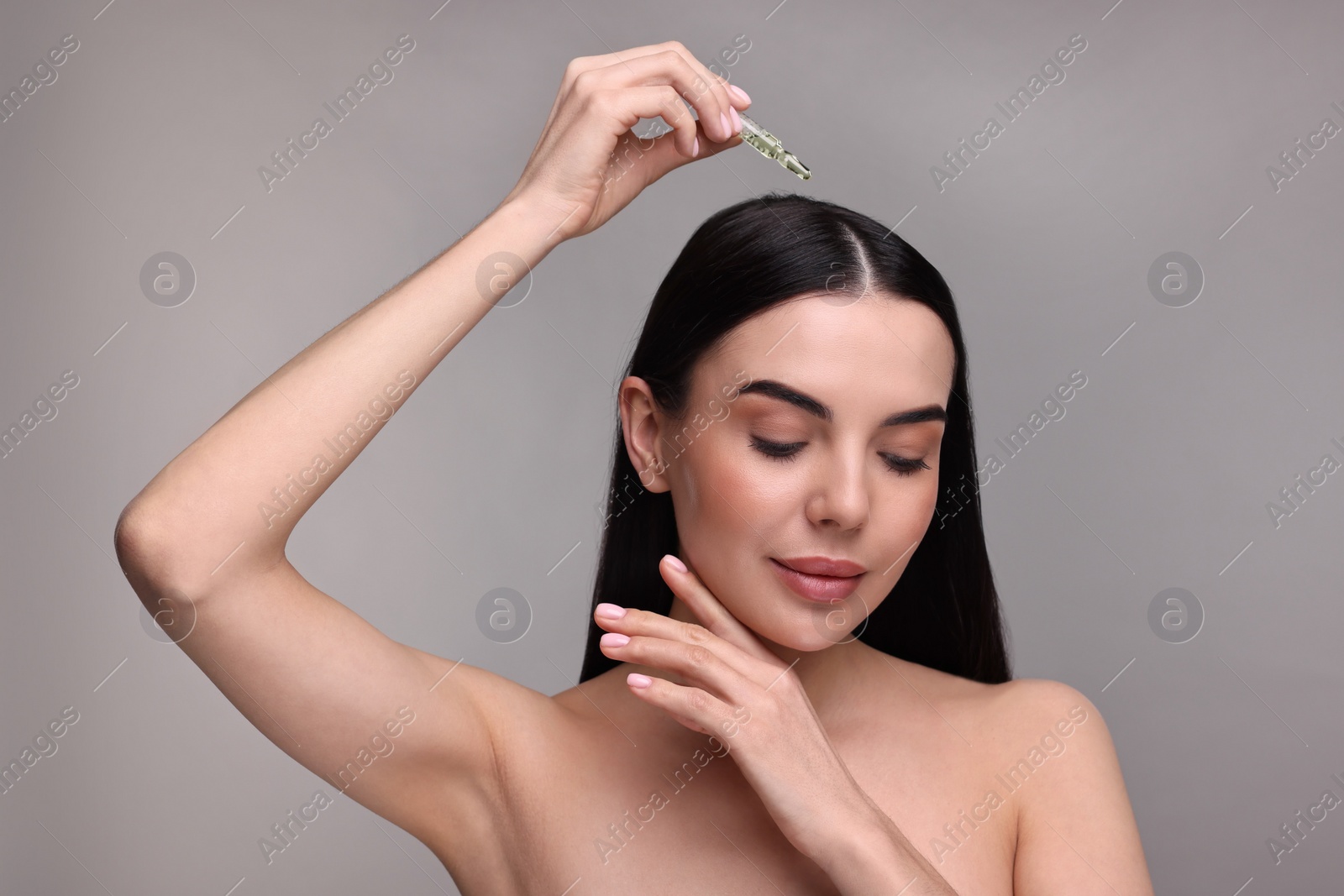 Photo of Beautiful young woman using ampoule for hair treatment on grey background