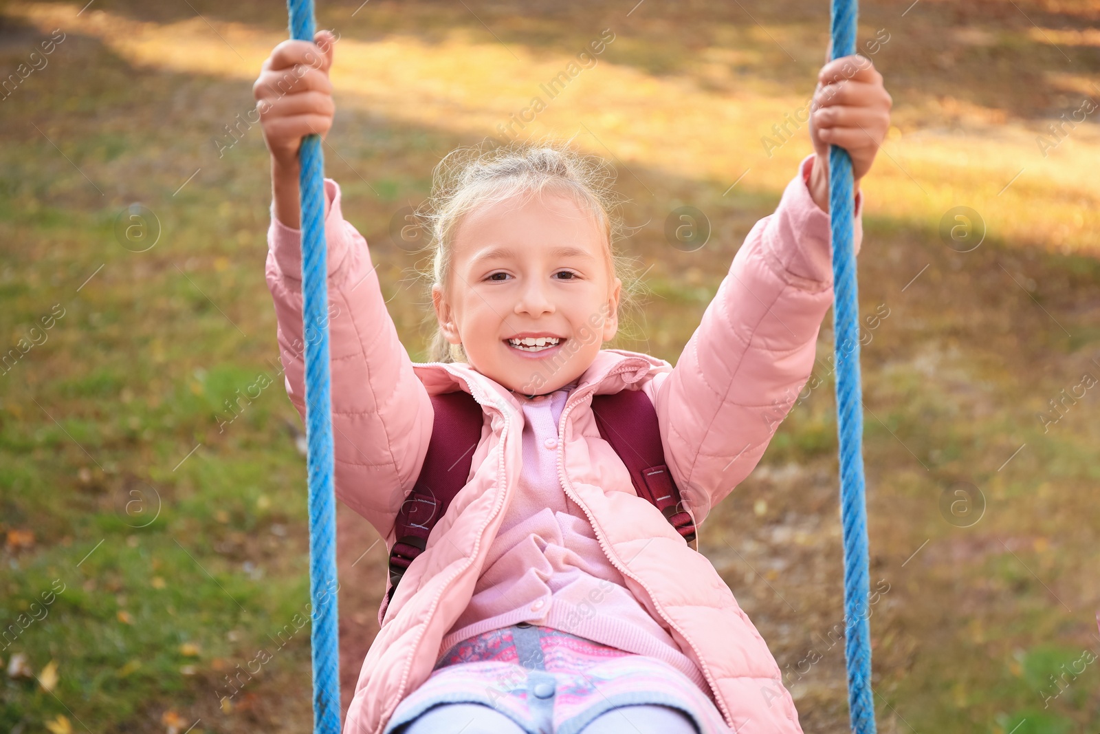 Photo of Cute little girl with backpack on swing outdoors