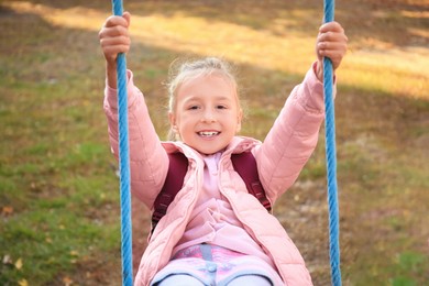 Cute little girl with backpack on swing outdoors