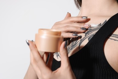 Photo of Woman applying healing cream onto her tattoos against light background, closeup