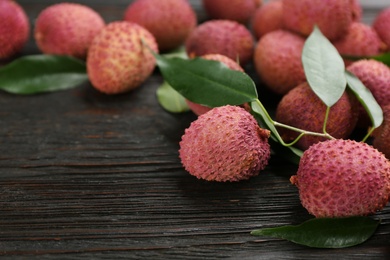 Photo of Fresh ripe lychee fruits on dark wooden table. Space for text