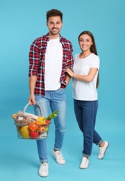 Young couple with shopping basket full of products on blue background