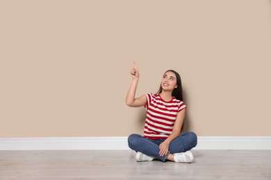 Young woman sitting on floor near beige wall indoors