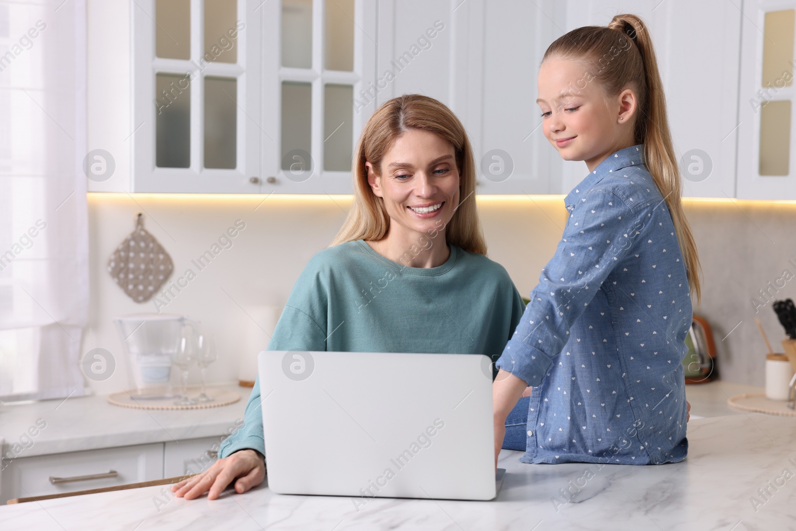 Photo of Happy woman and her daughter with laptop at white table indoors